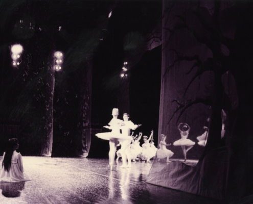 A ballerina sits on stage, watching dancers in white tutus perform under soft spotlight. Curtains depict trees, enhancing a whimsical, serene atmosphere.